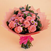 Coral Rose Whisper bouquet with coral roses, mauve daisy-style blooms, eucalyptus, coral wrapping, and pink ribbon by Rapid Petals by Yashken Fresh